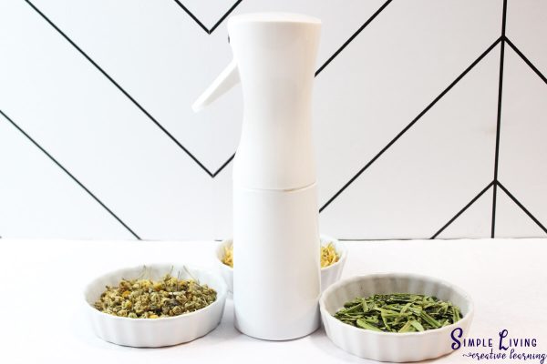 Homemade Jewelweed Spray in a white spray bottle with herbs and flowers in bowls