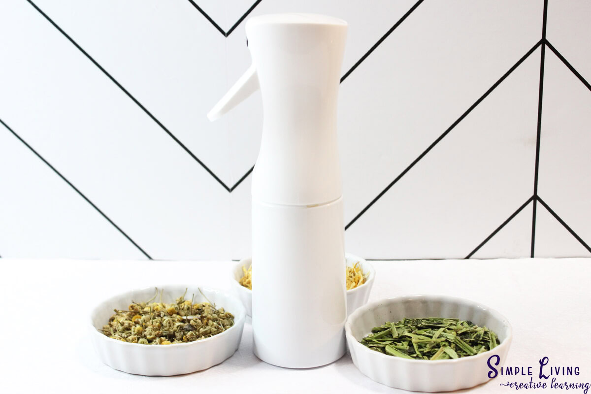 Homemade Jewelweed Spray in a white spray bottle with herbs and flowers in bowls